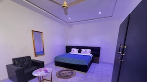 A bedroom with a bed, a black sofa, a small table, a mirror, and a wardrobe.