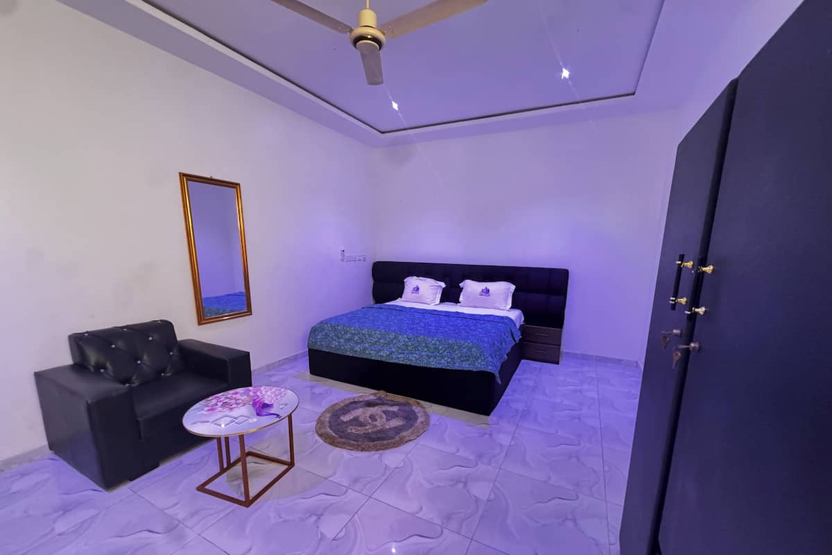 A bedroom with a bed, a black sofa, a small table, a mirror, and a wardrobe.