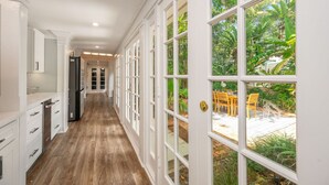 Un pasillo con piso de madera, muebles blancos y ventanas grandes que dan a un patio.