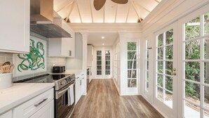 Una cocina amplia con armarios blancos, piso de madera y ventanas grandes.