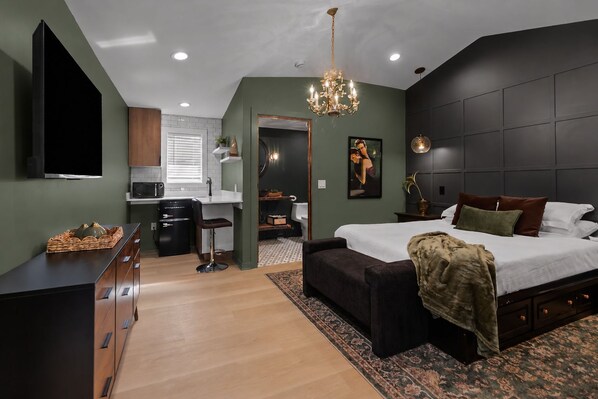Un dormitorio moderno con una cama grande, televisión, kitchenette y baño.