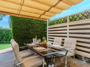 Une terrasse extérieure avec une table dressée pour le repas, entourée de chaises, et protégée par un auvent.