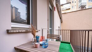 A balcony with a wooden table, a chair, a small rug, and a window overlooking a building. - Glam Turin Apartment, in the heart of San Salvario, a stone's throw from downtown (Torino)