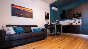 A modern living room with a dark brown sofa, a wooden floor, and a cityscape painting on the wall. - Glam Turin Apartment, in the heart of San Salvario, a stone's throw from downtown (Torino)