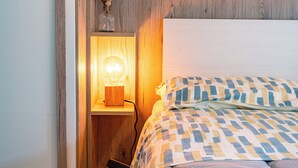 A bedroom with a bed, a bedside lamp, a wooden shelf with decorative items, and a wardrobe. - Glam Turin Apartment, in the heart of San Salvario, a stone's throw from downtown (Torino)