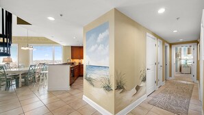 Une cuisine moderne avec vue sur la ville, un coin repas offrant également une vue panoramique, et un couloir décoré d’une fresque représentant une plage.