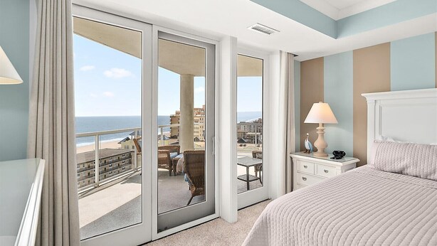 Une chambre d’hôtel avec un lit, une table de chevet, une lampe, une chaise et une vue sur la plage.