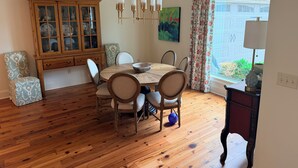 A dining area with a wooden table, chairs, a cabinet with glass doors, and a painting on the wall. - Grand Oaks 6BR by Country Club - Sleeps 12 + Crib - Sauna, Pizza Oven, Ole Miss (Oxford)