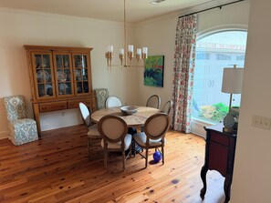 A dining area with a wooden table, chairs, a cabinet with glass doors, and a painting on the wall. - Grand Oaks 6BR by Country Club - Sleeps 12 + Crib - Sauna, Pizza Oven, Ole Miss (Oxford)