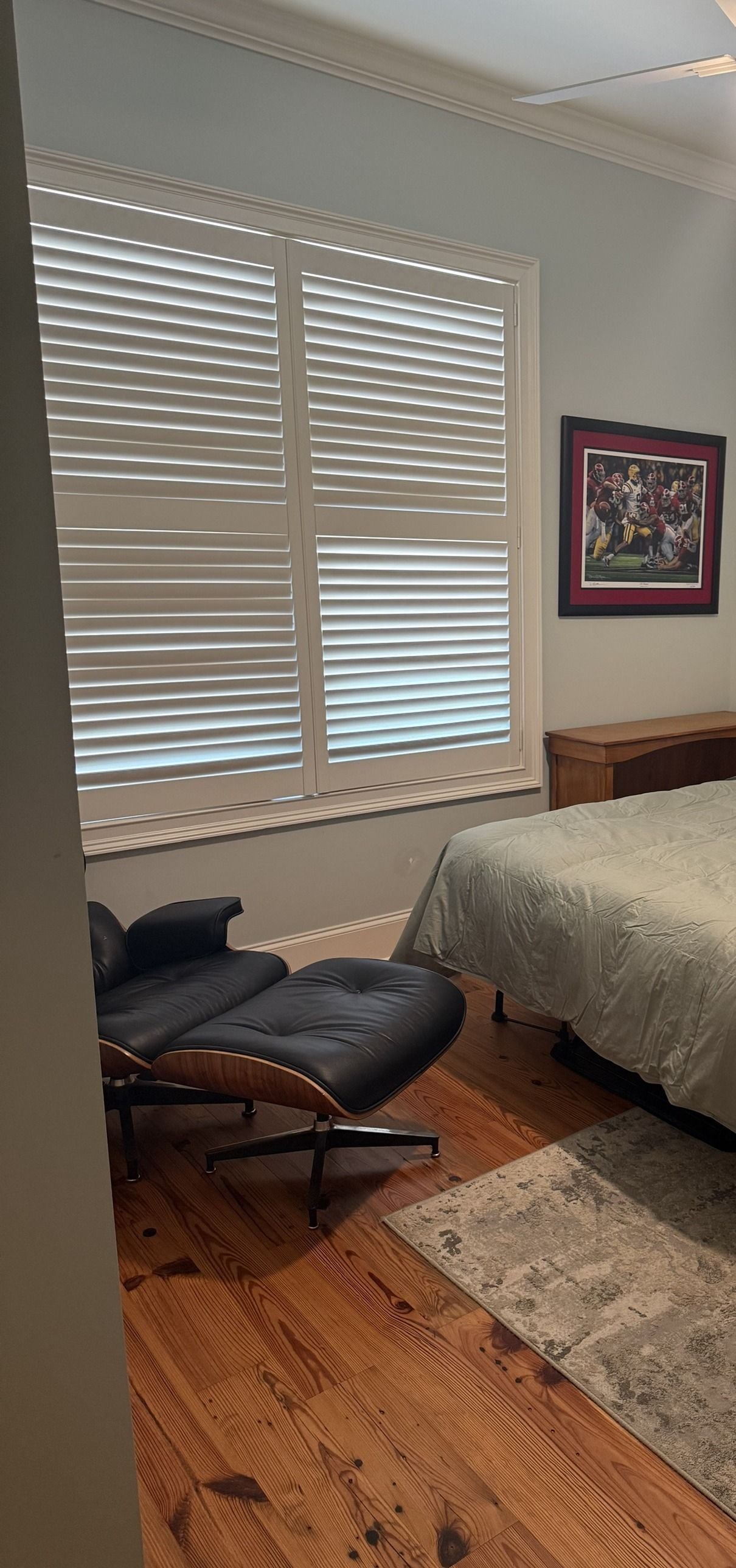 A bedroom with a bed, a chair, a window with blinds, a framed picture on the wall, and a rug on the floor.