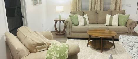 A living room with a sofa, a coffee table, and a chair. There is a lamp on a side table, and a ceiling fan.