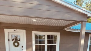 Ett hus med en vit dörr, ett fönster dekorerat med en krans och två stolar under en överbyggd veranda.