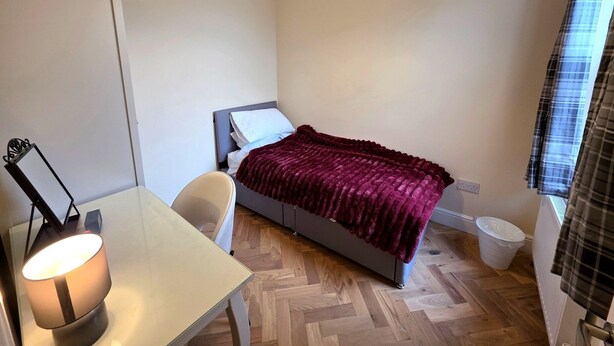 Ein kleines, ordentliches Schlafzimmer mit einem Bett, einem Schreibtisch und einem Sessel.