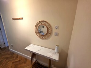 A hallway with a white marble console table, a round mirror with a woven frame, and a light switch. - Spacious 5BDR Home in Walthamstow Village (Greater London)