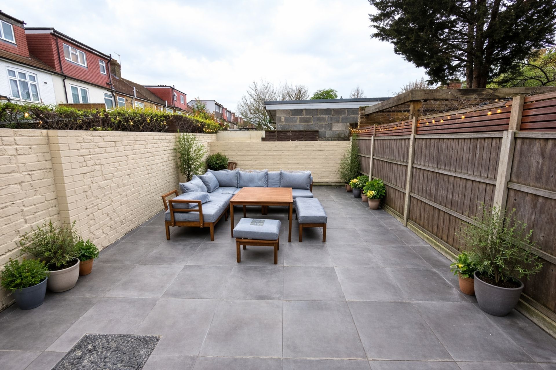 A patio with a wooden table and a sofa set, surrounded by potted plants and a brick wall.