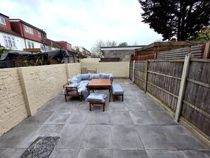A patio area with a built-in seating arrangement, a wooden table, and a brick wall. - Spacious 5BDR Home in Walthamstow Village (Greater London)