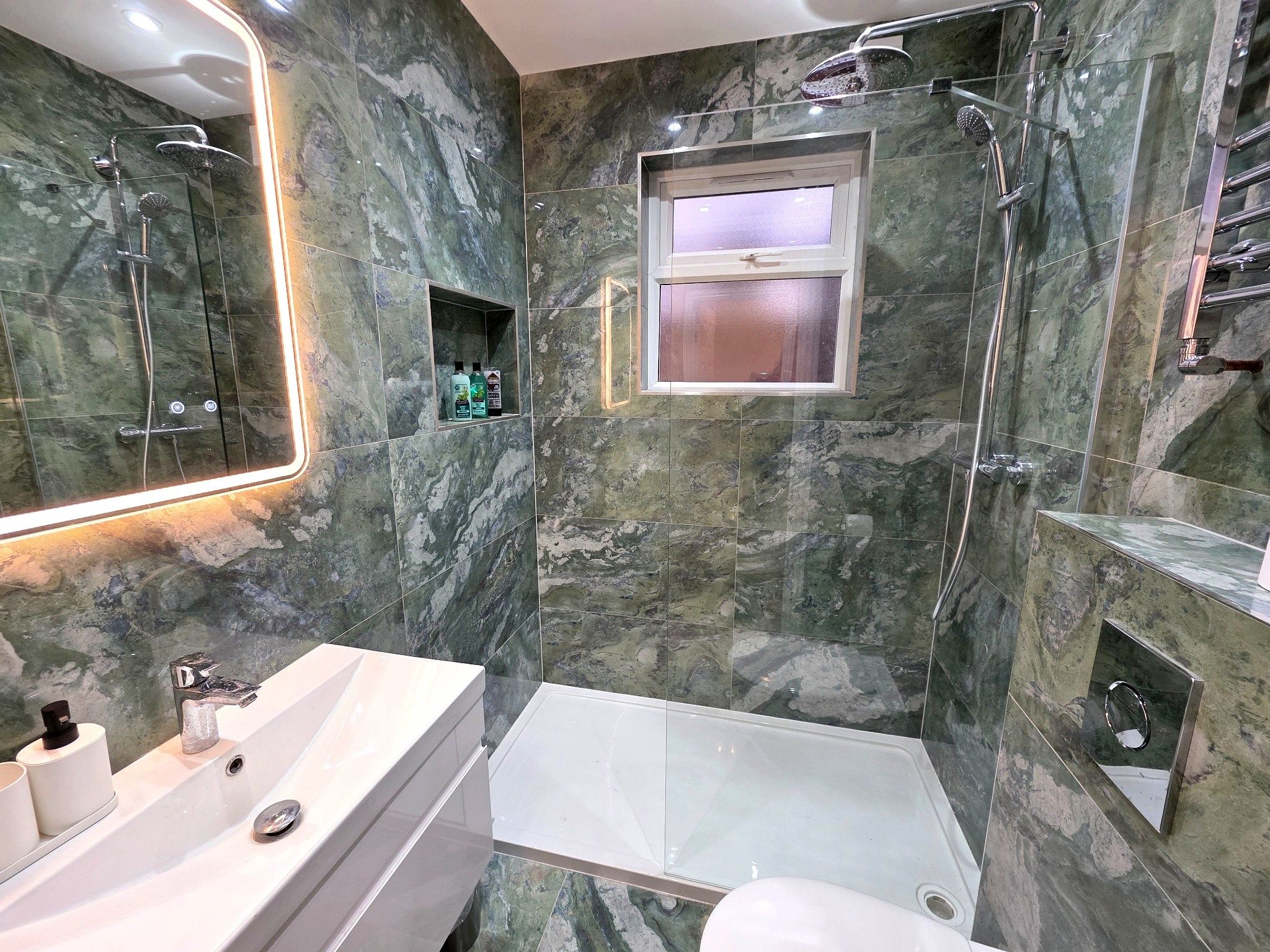 A bathroom with a glass-enclosed shower, a sink with a mirror, and a window above the toilet.