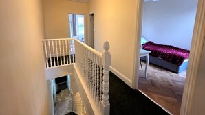 Eine Treppe mit weißen Balustraden führt zu einem Schlafzimmer mit einem Bett und einem Sessel.