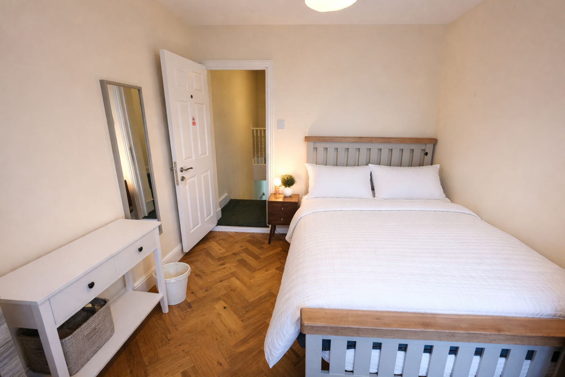 Une chambre à coucher comprenant un lit, une table de chevet, une commode, un miroir et une porte donnant sur une autre pièce.