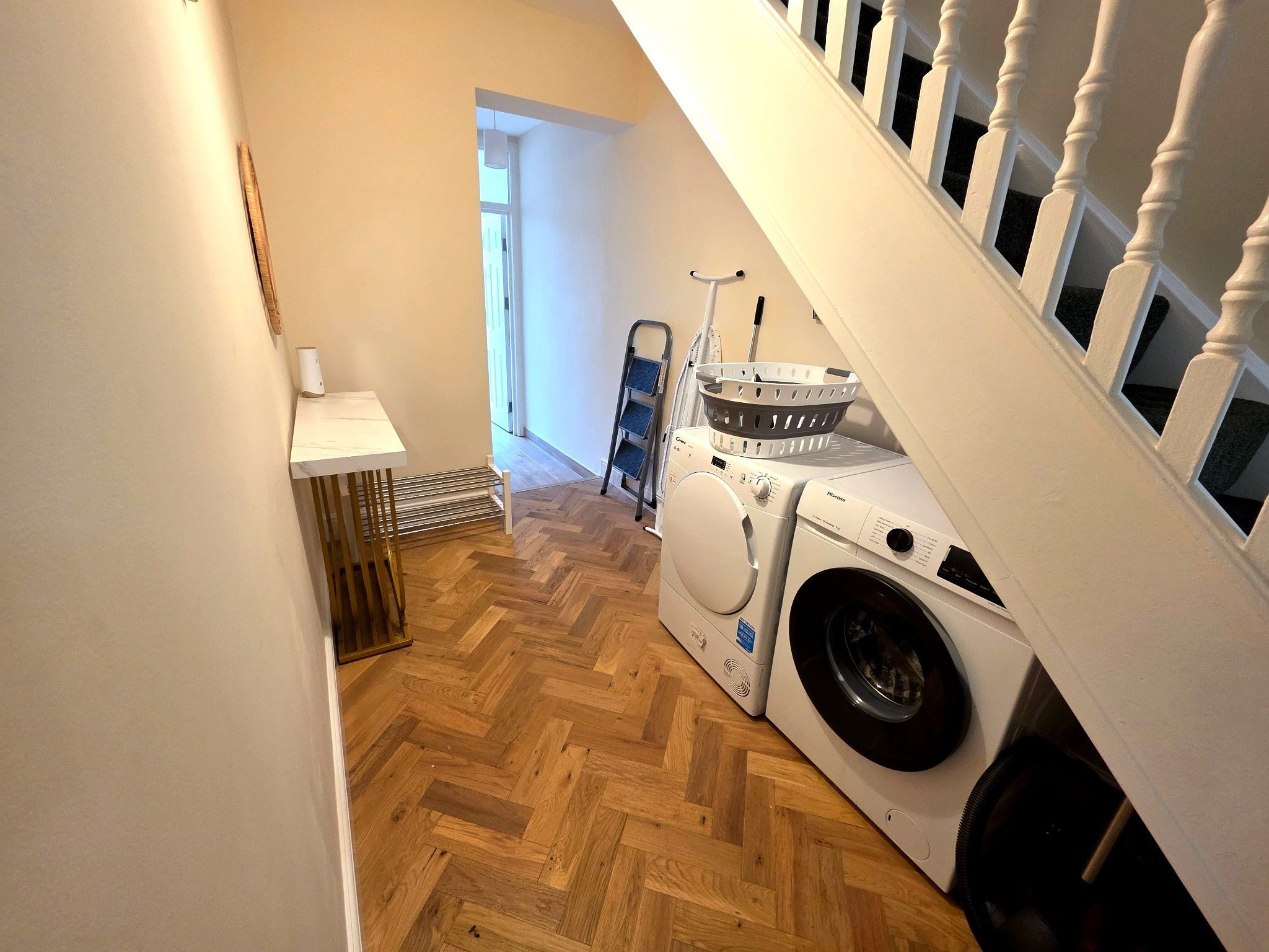 A laundry area with a washing machine and dryer, a drying rack, and a small table with a lamp.