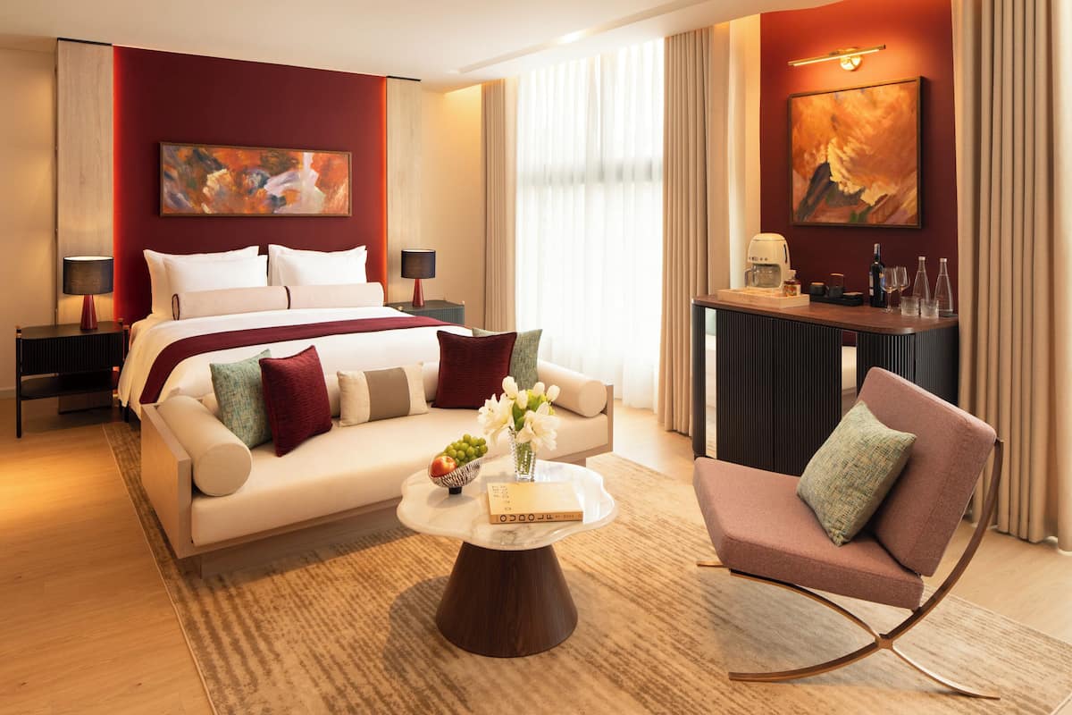 Een hotelkamer met een bed, een slaapbank, een salontafel, een stoel, een bureau en kunstwerken aan de muur.