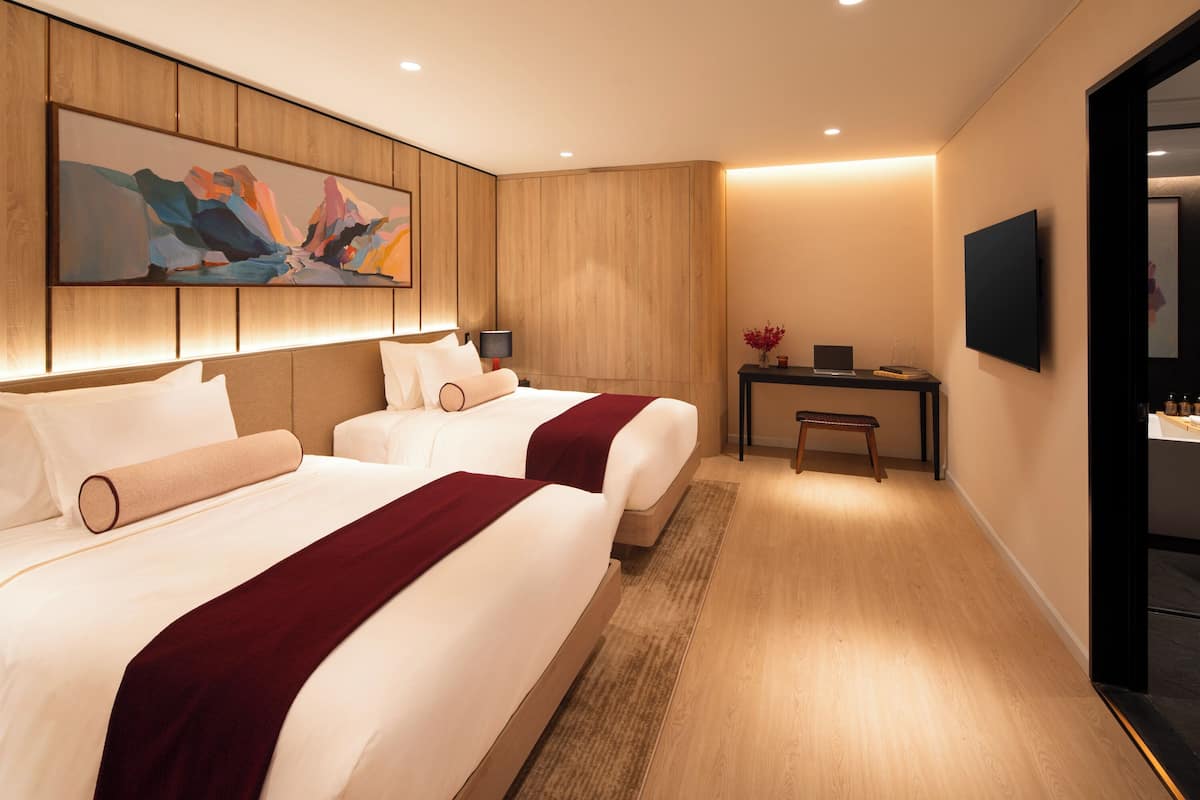 Een hotelkamer met twee bedden, een bureau, een stoel, een flatscreen televisie en een schilderij aan de muur.