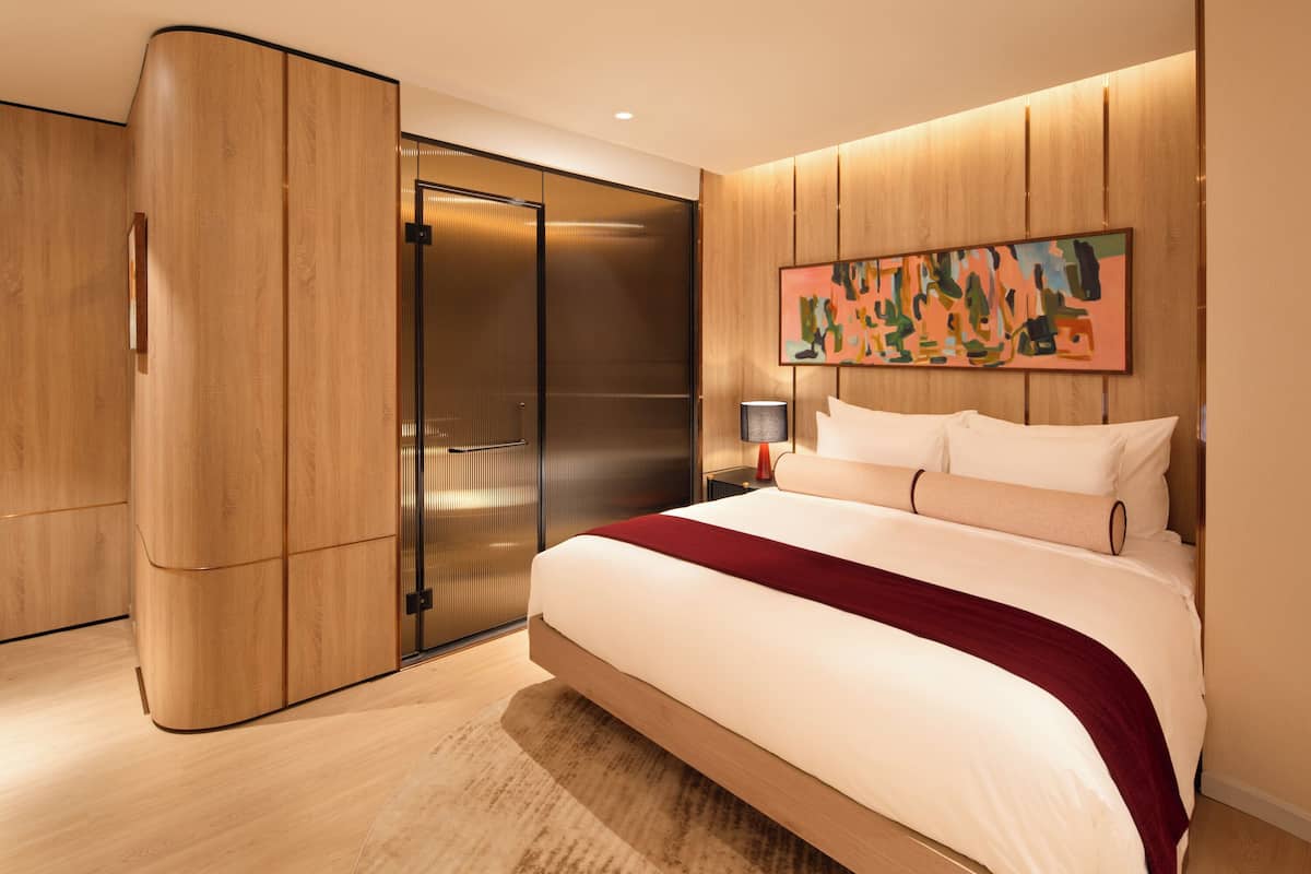 Een moderne slaapkamer met een groot bed, houten lambrisering, een schuifdeurkast en een kleurrijk abstract schilderij aan de muur.