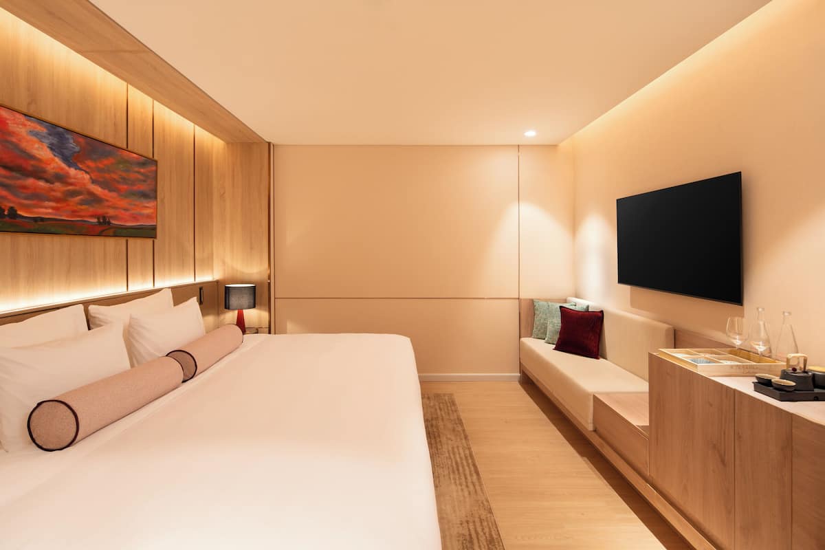 Een moderne hotelkamer met een groot bed, een flatscreen televisie, een houten hoofdbord en een schilderij aan de muur.