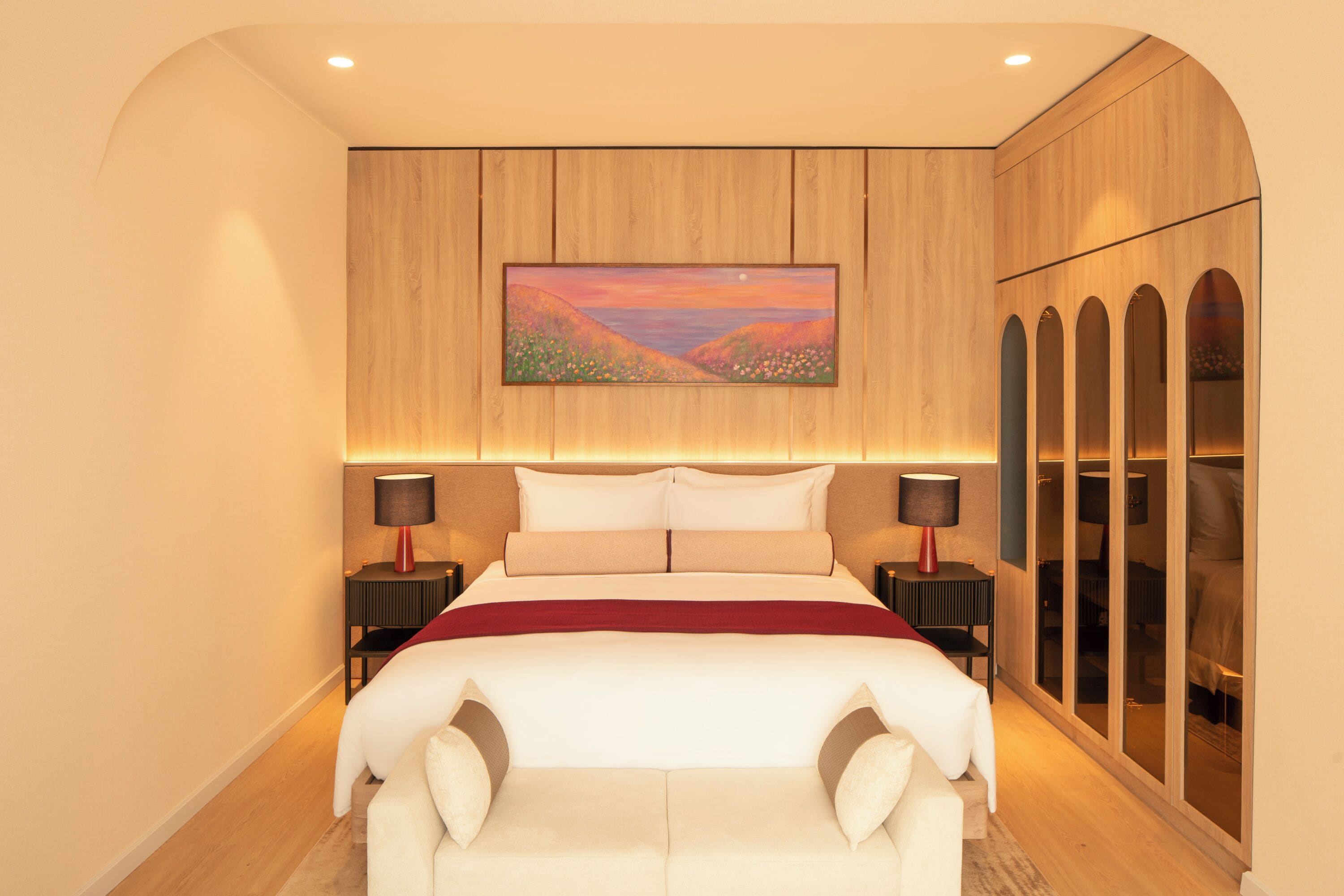 A bedroom with a bed, a painting, a wardrobe, and a nightstand with a lamp.