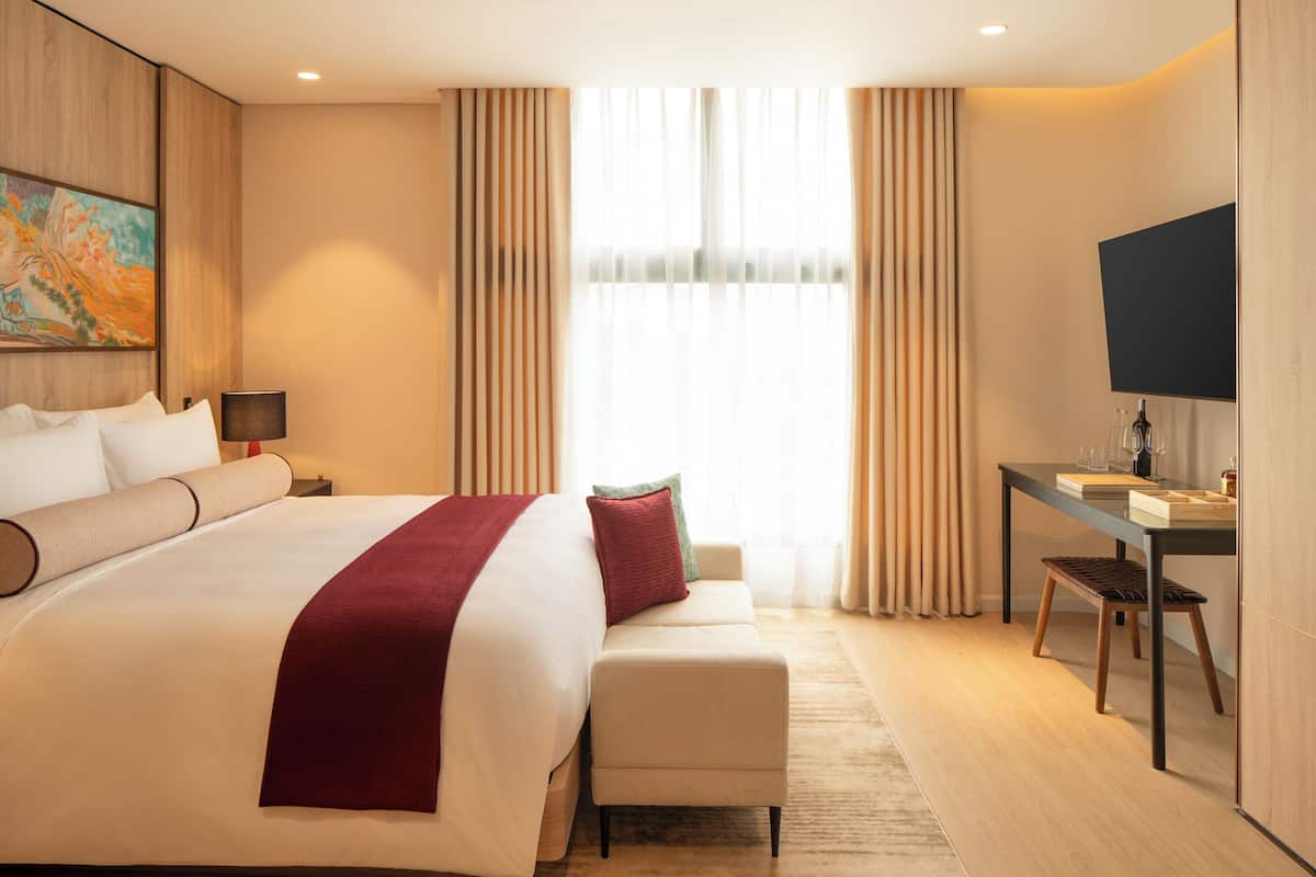 Een hotelkamer met een groot bed, een bureau, een stoel, een televisie en een schilderij aan de muur.