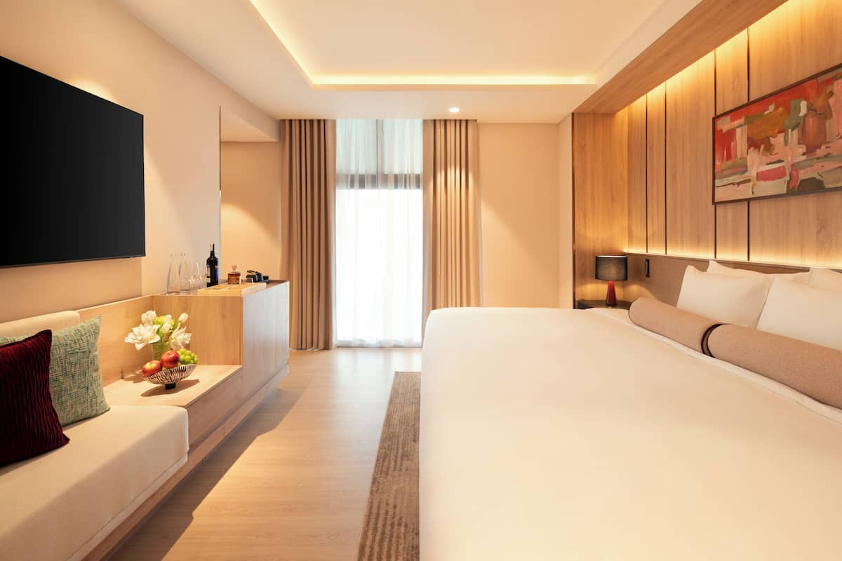 Een moderne hotelkamer met een groot bed, een zithoek met televisie en een bureau met een bloevas.