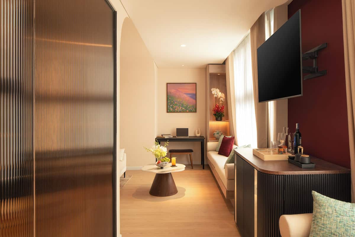 Een moderne woonkamer met een flatscreen televisie, een ronde salontafel met bloemen, een bank, een bureau met een laptop en een rode accentmuur.