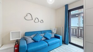 Una habitación con un sofá azul, decoración en forma de corazón en la pared, un radiador blanco y un extintor.