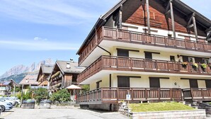 Un hotel de varios pisos con balcones, un estacionamiento y montañas al fondo.