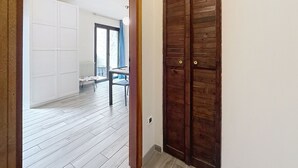 Un pasillo con una puerta de madera, un armario blanco y vistas a una habitación con una mesa y sillas.
