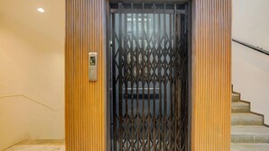 Una puerta con una reja de metal, un interruptor de luz y una escalera a la derecha.