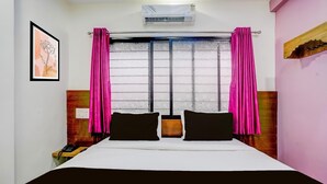 Habitación de hotel con cama, mesita de noche, teléfono, ventana con cortinas, aire acondicionado y una obra de arte colgada en la pared.