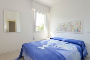 A bedroom with a bed, a window, a door, and a wall-mounted artwork. - Lignano Sabbiadoro Flat With Parking (Lignano Sabbiadoro)
