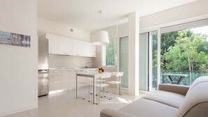 Een moderne keuken met witte kastjes, een eethoek met tafel en stoelen, en een grote schuifpui naar een balkon.
