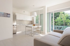 Eine moderne Küche mit weißen Schränken, ein Essbereich mit Tisch und Stühlen sowie eine große Schiebeglasdoor zu einem Balkon.
