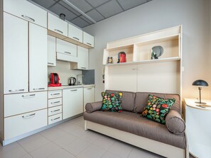 A compact living space with a kitchenette, sofa, and a small table with a lamp. - Domus Talenti by Interhome (Alba)