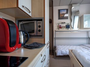 A compact kitchenette with a microwave, kettle, and a red appliance, a bunk bed with a white mattress, and a small shelf with books and a picture frame. - Domus Talenti by Interhome (Alba)