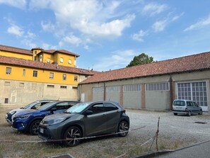 A parking area with a chain-locked car, a building with a tiled roof, and a clear sky. - Domus Talenti by Interhome (Alba)