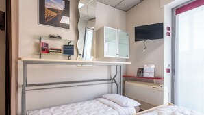 Hotellihuone, jossa on sänky, työpöytä tietokoneella, televisio ja ikkuna, jossa on sälekaihtimet.