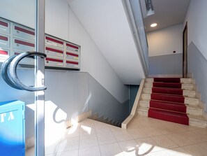 A staircase with red carpeted steps, a metal handrail, and a wall-mounted information board. - Domus Talenti by Interhome (Alba)