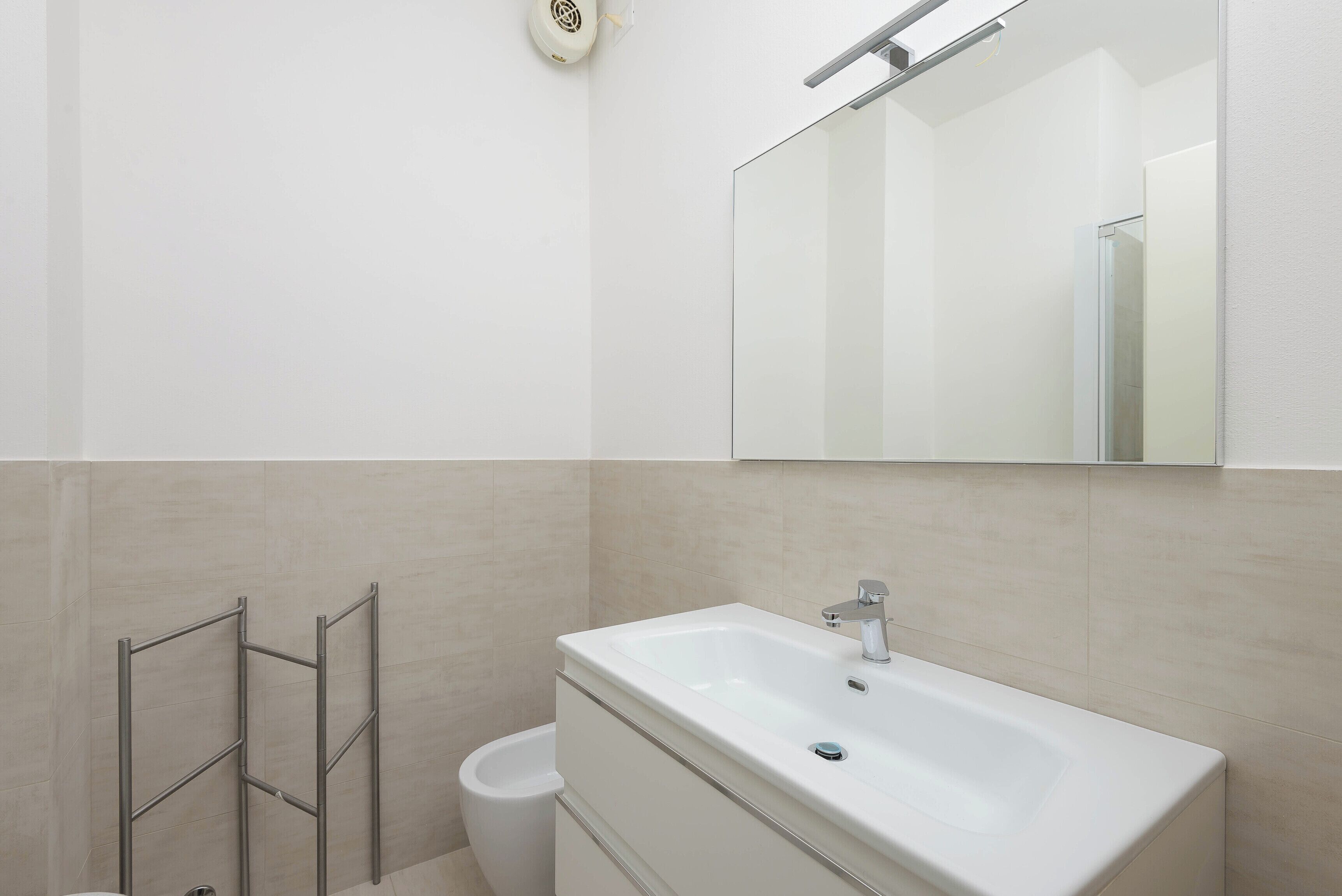A modern bathroom with a white sink, mirror, and towel rack.