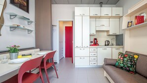 A compact living space with a dining area, kitchenette, and a sofa with a floral pillow. - Domus Talenti by Interhome (Alba)
