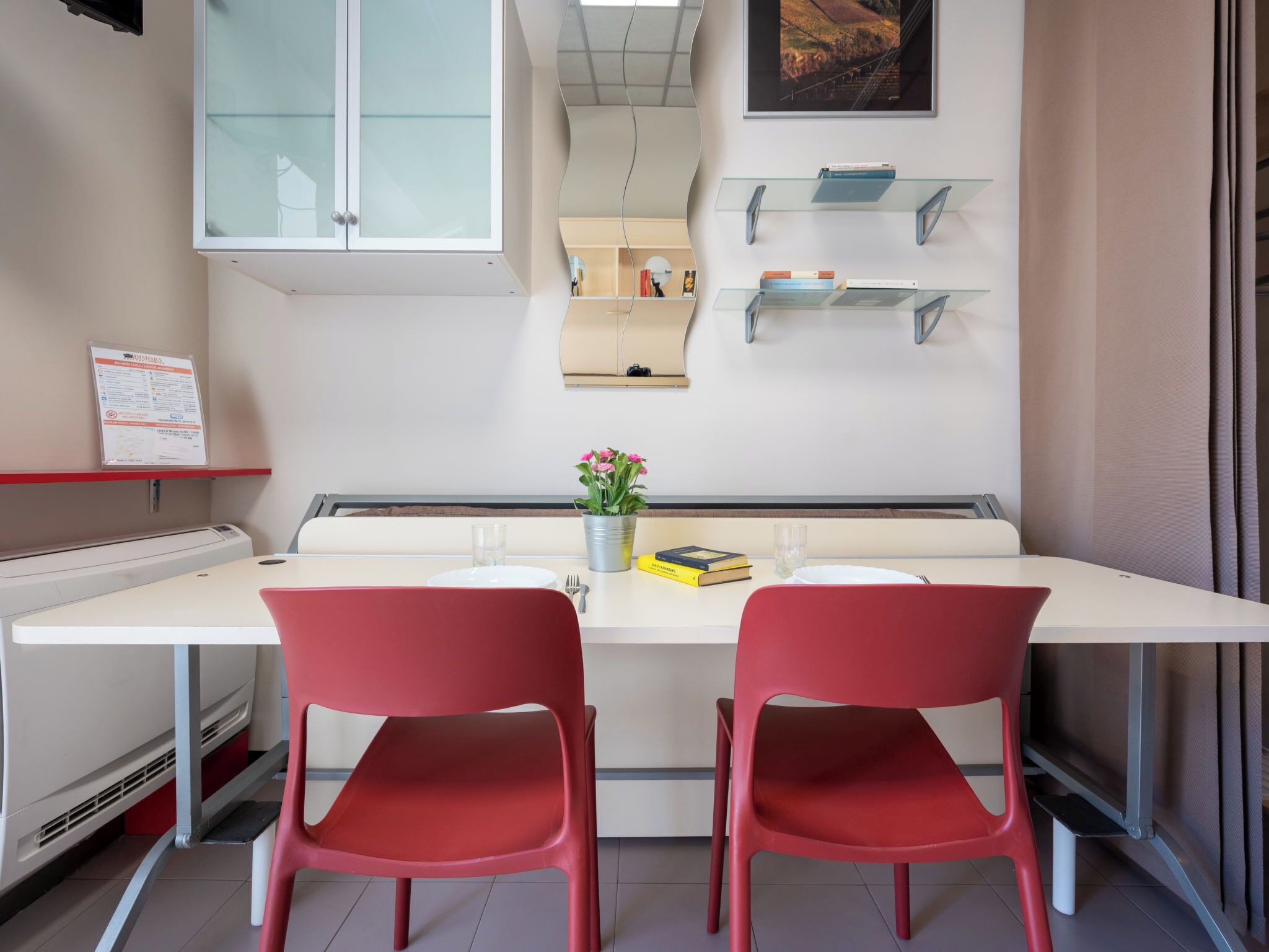 Una stanza con una scrivania bianca, due sedie rosse, una pianta in vaso e un quadro appeso al muro.