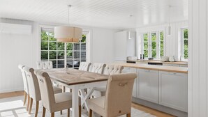 A modern kitchen with white cabinetry, a wooden dining table, and a large window. - "Har" - 685m from the sea by Interhome (Hornbæk)