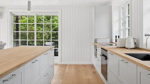 A modern kitchen with white cabinetry, wooden countertops, a large window, and a view of greenery. - "Har" - 685m from the sea by Interhome (Hornbæk)